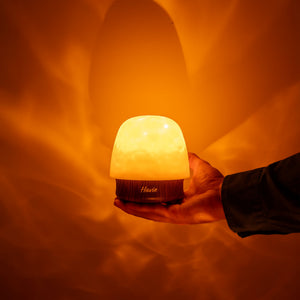 Den oppladbare nattlampen Havie holdes i en hånd og sprer et varmt oransje lys.