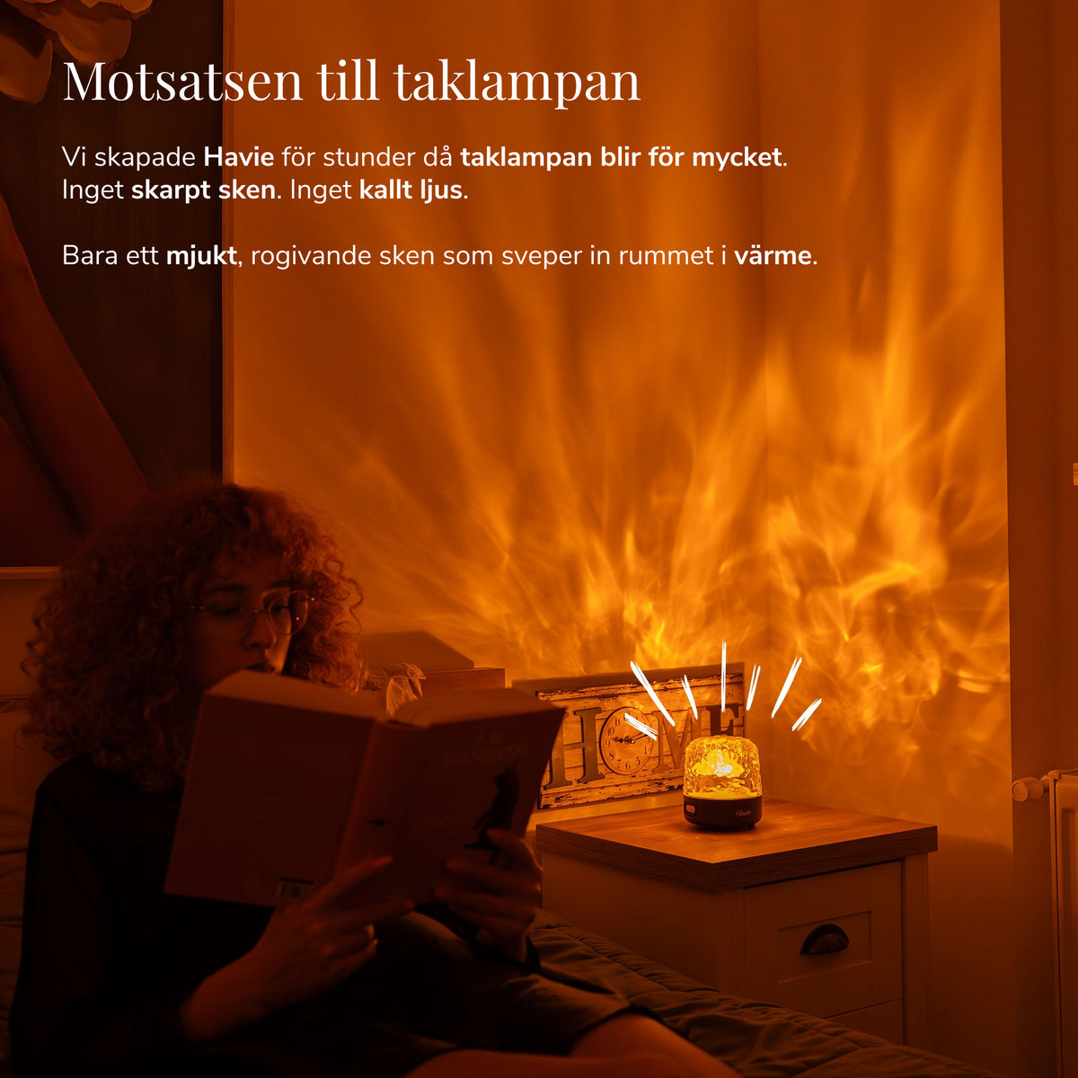En kvinna läser bredvid Havie, som sprider ett varmt orange sken i ett ombonat sovrum.