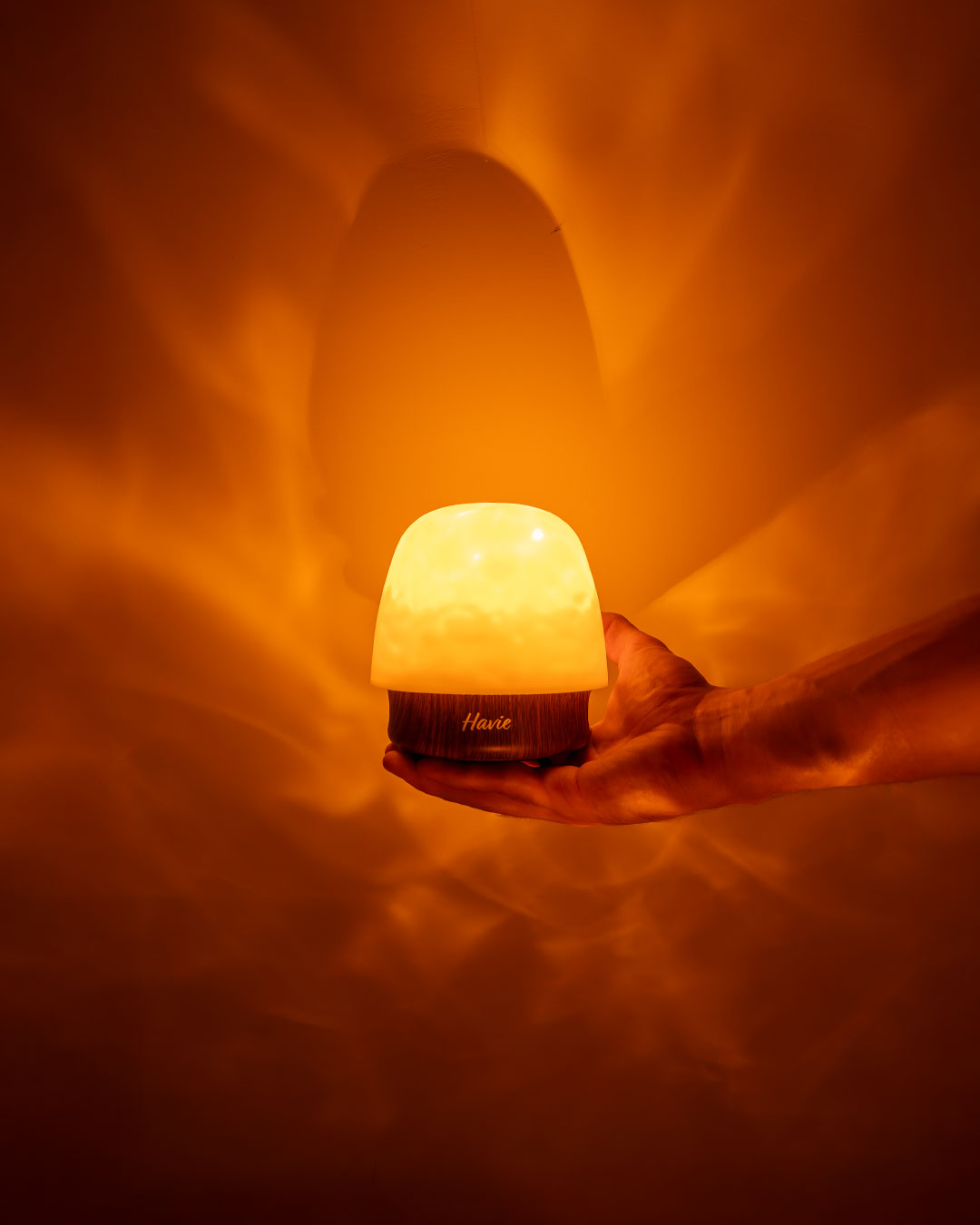 Havie-lampen i en åben hånd med et varmt orange skær på væggen bagved