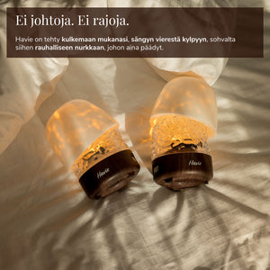 Kaksi johdotonta, ladattavaa Havie-lamppua hohtaa lämpimästi sängyllä.