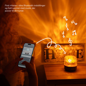 En person forbinder mobilen til Havie via Bluetooth, mens lampen fylder rummet med varmt lys.